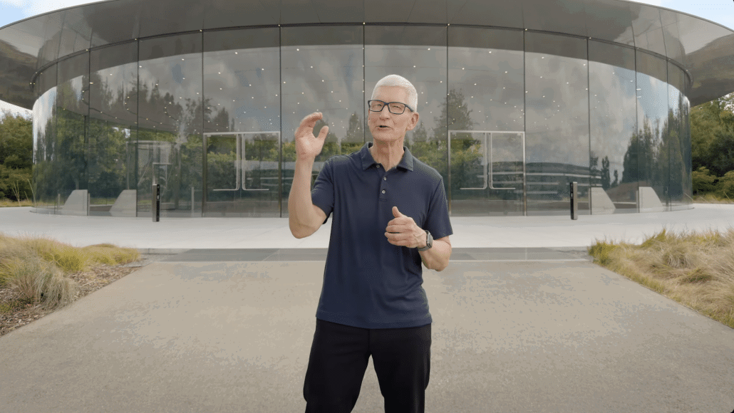 Apple Chef Tim Cook spricht vor modernem Glasgebäude.