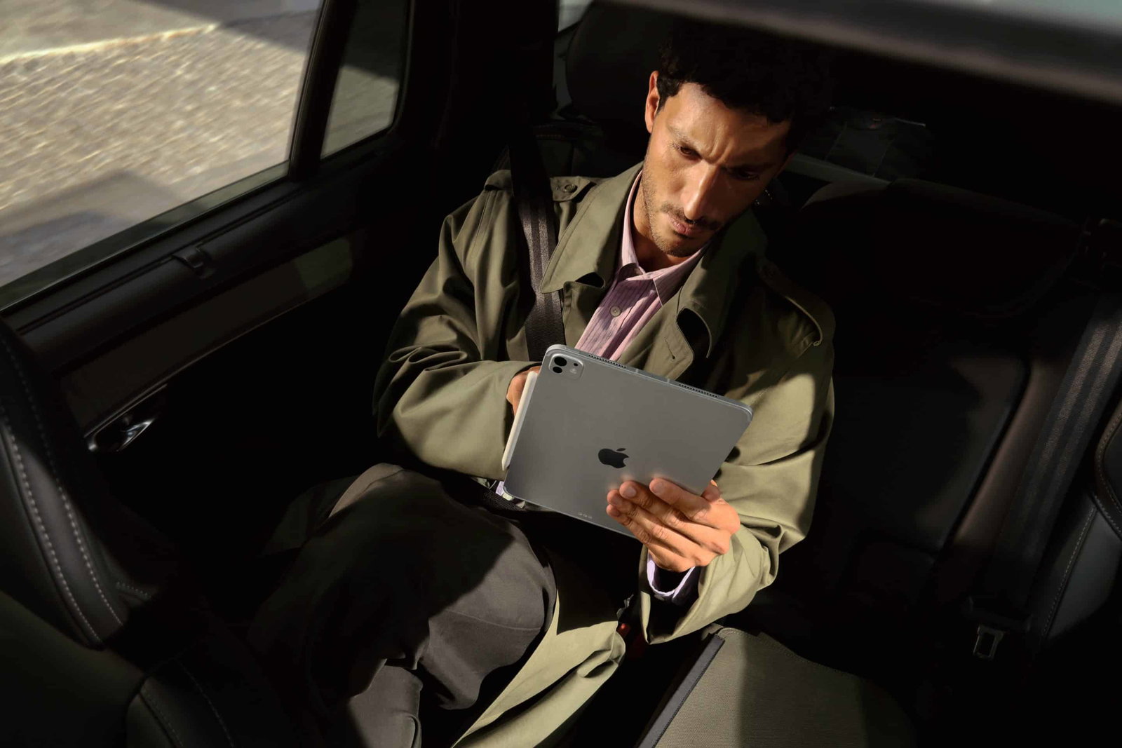 Mann sitzt im Auto und nutzt ein iPad.