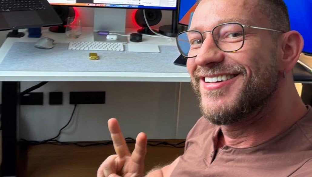 Lächelnder Mann zeigt Friedenstecken vor Computer